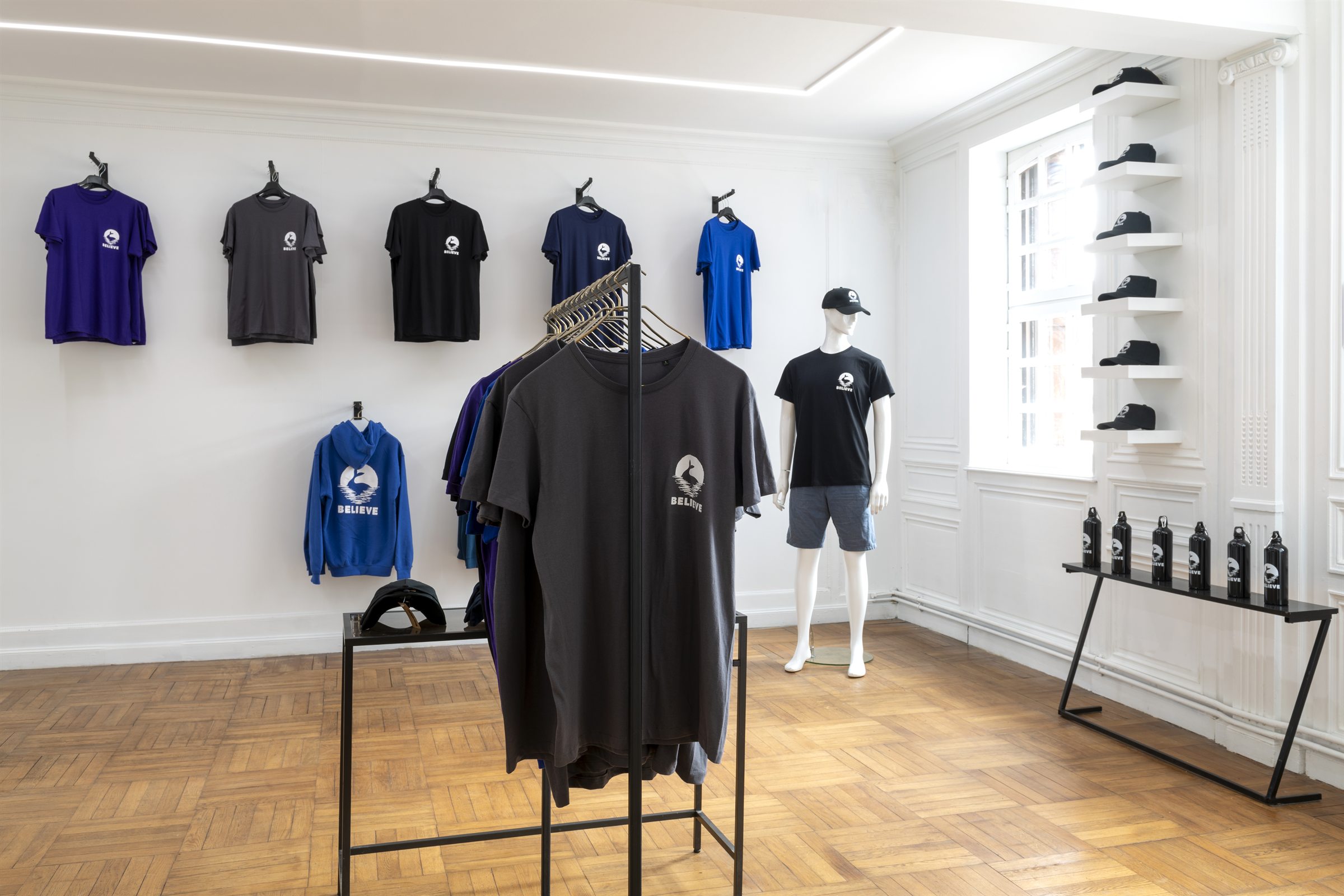 Salle de l'exposition Believe : t-shirts, sweat et casquettes au logo Believe, mannequin et gourdes