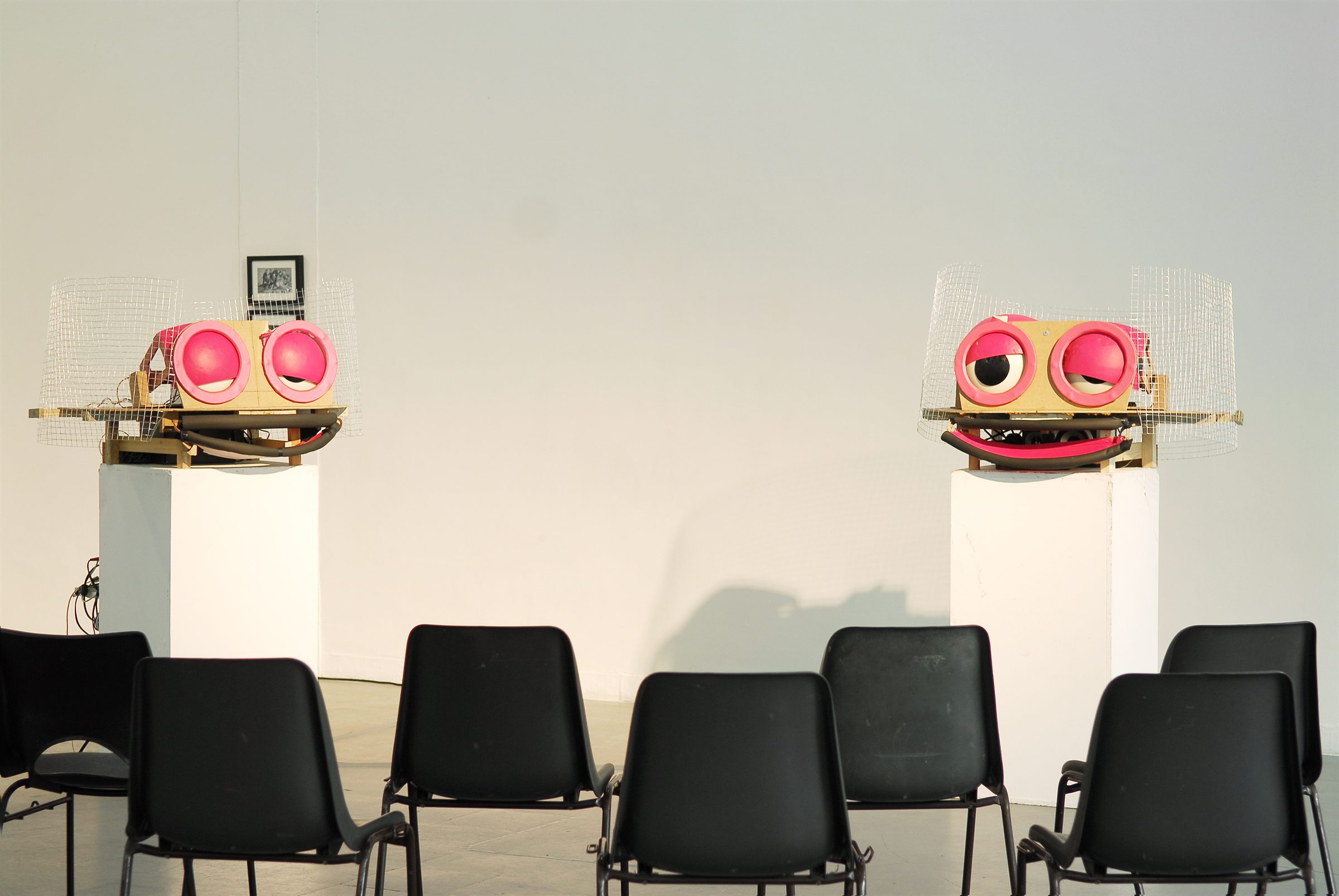 Les deux têtes robotiques de Jacques face à des rangées de chaises, dans l'exposition Dieu et la Stéréo